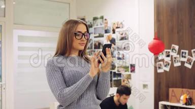 戴眼镜的年轻女人在办公室里使用智能手机。 短信，网上冲浪，APP，社交网络..